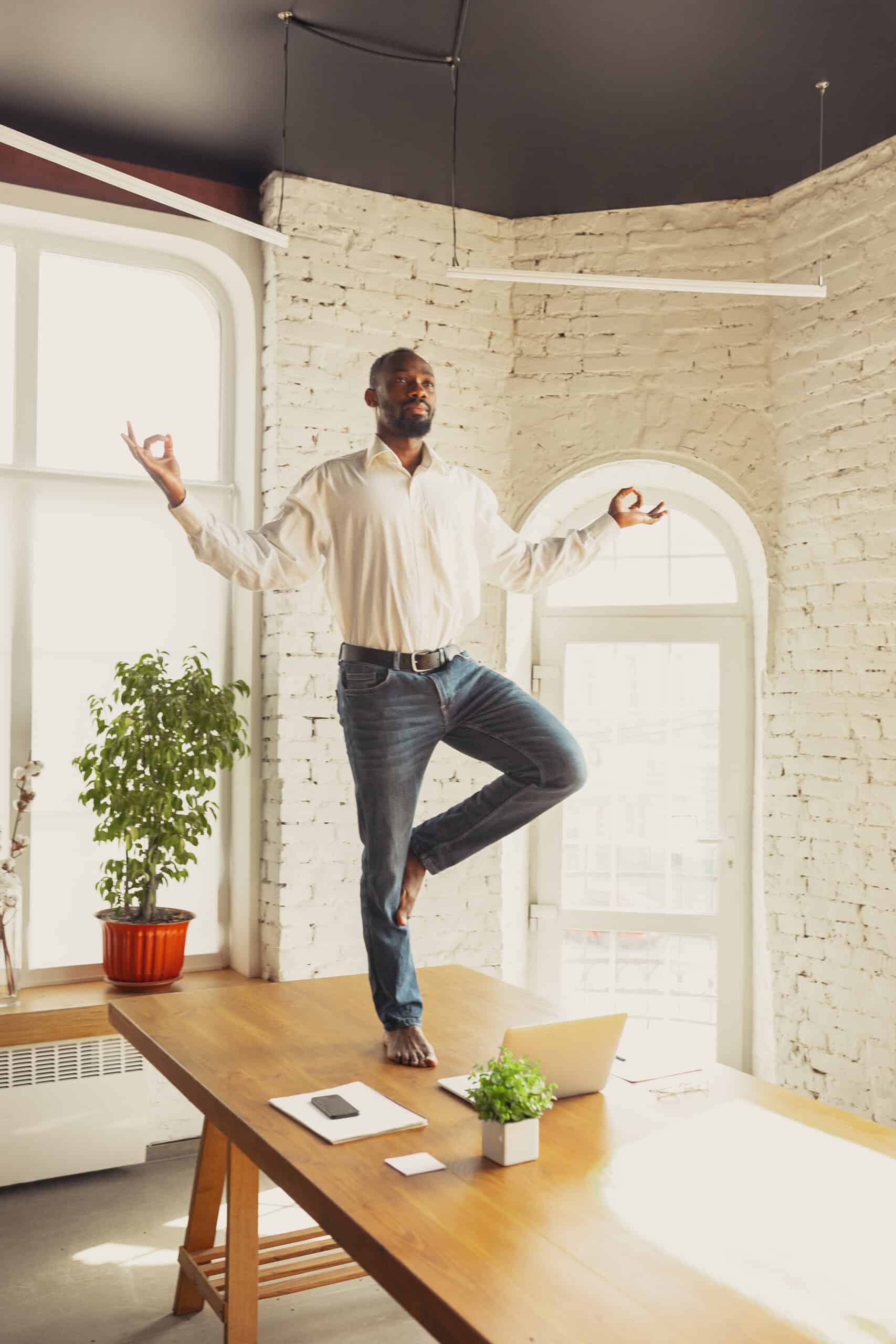 Young African-american man doing tree pose on his desk