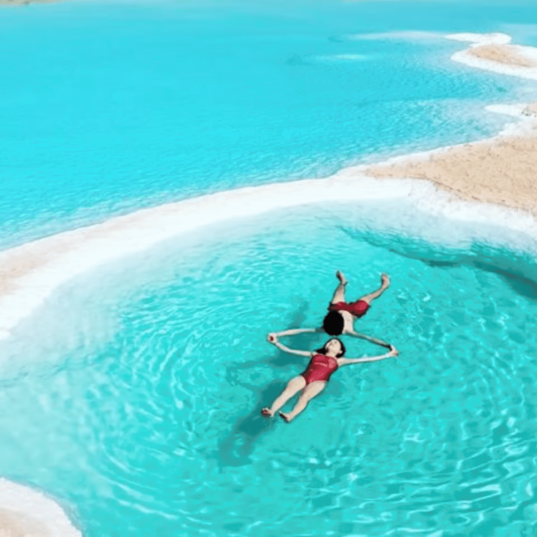 Two people floating in clear turquoise waters of a natural pool with white sandy edges.