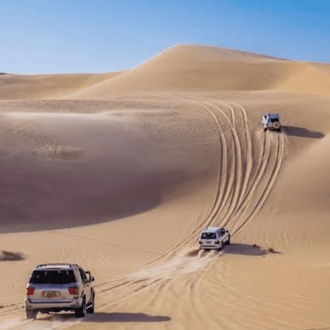 Three SUVs driving through desert sand dunes, leaving tire tracks behind.