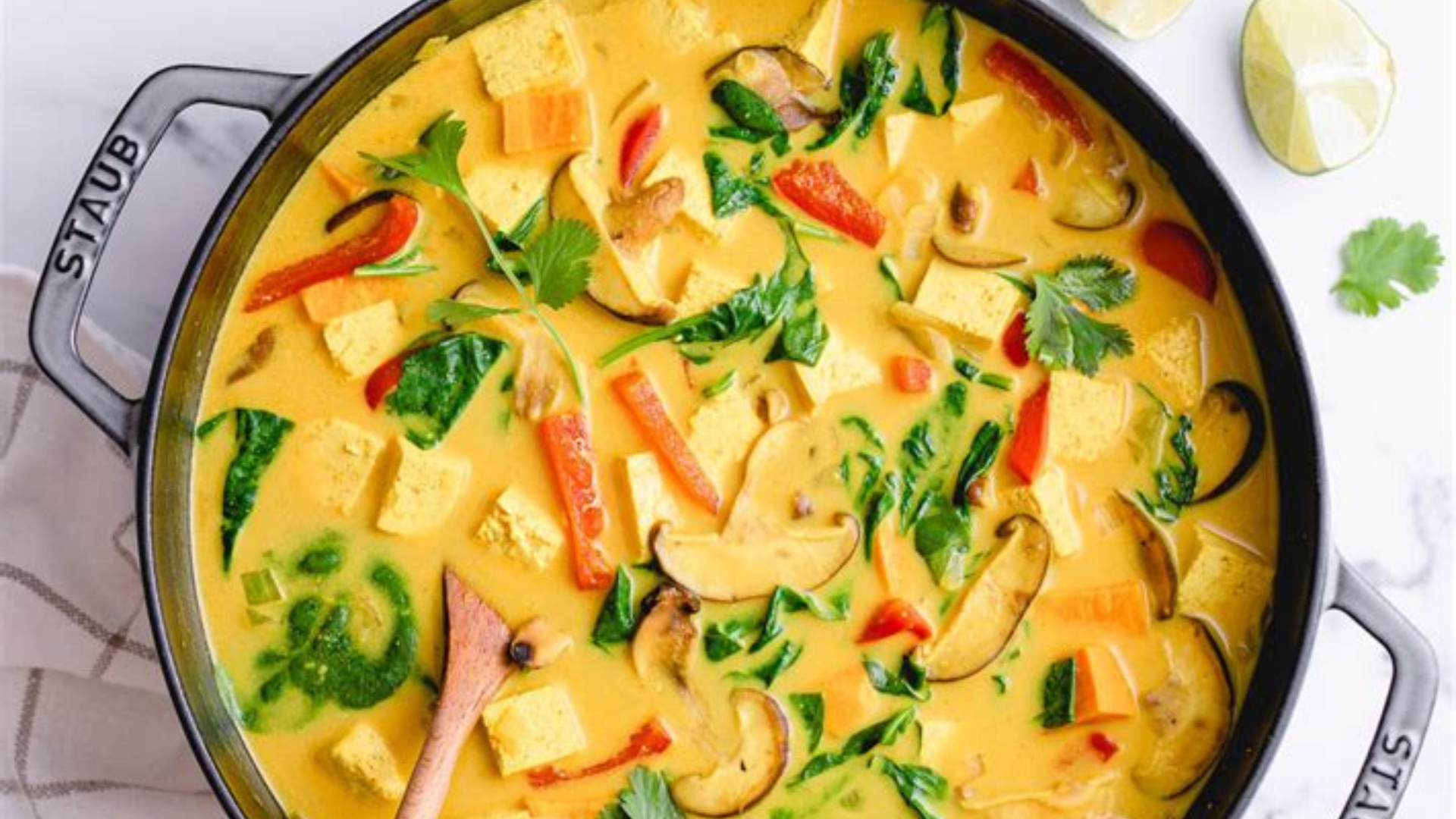 rainbow yellow curry with tofu, red peppers, mushrooms, spinach, and herbs in a black .